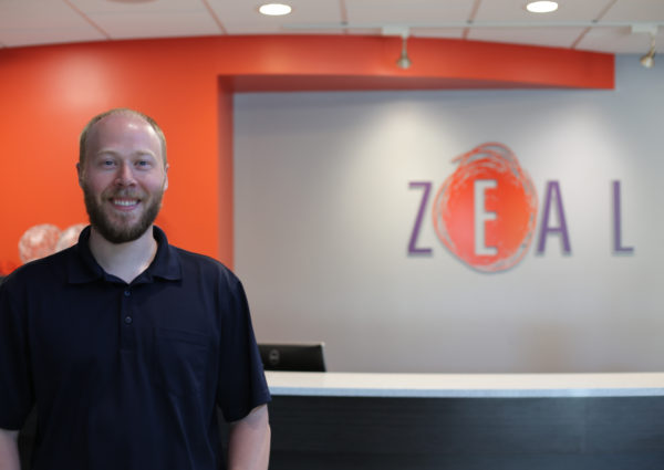 Trevor Weinrich standing in front of Zeal sign
